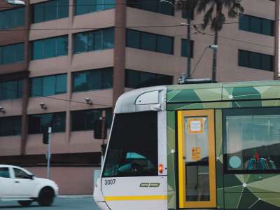 white and green tram travelling past corner of pink building and traffic lights